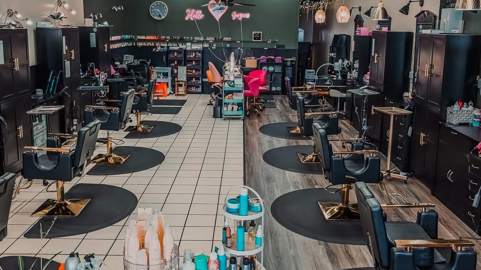 The Hello Gorgeous studio floor, with black stations, gold chairs, and the pink neon sign on the back wall.